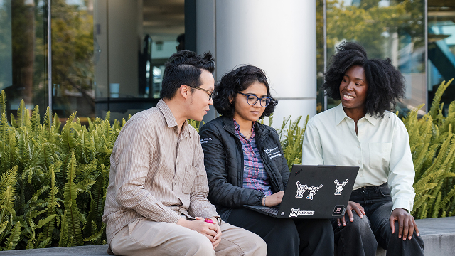 Three Marvell employees sit outside huddled over a laptop surrounded by greenery